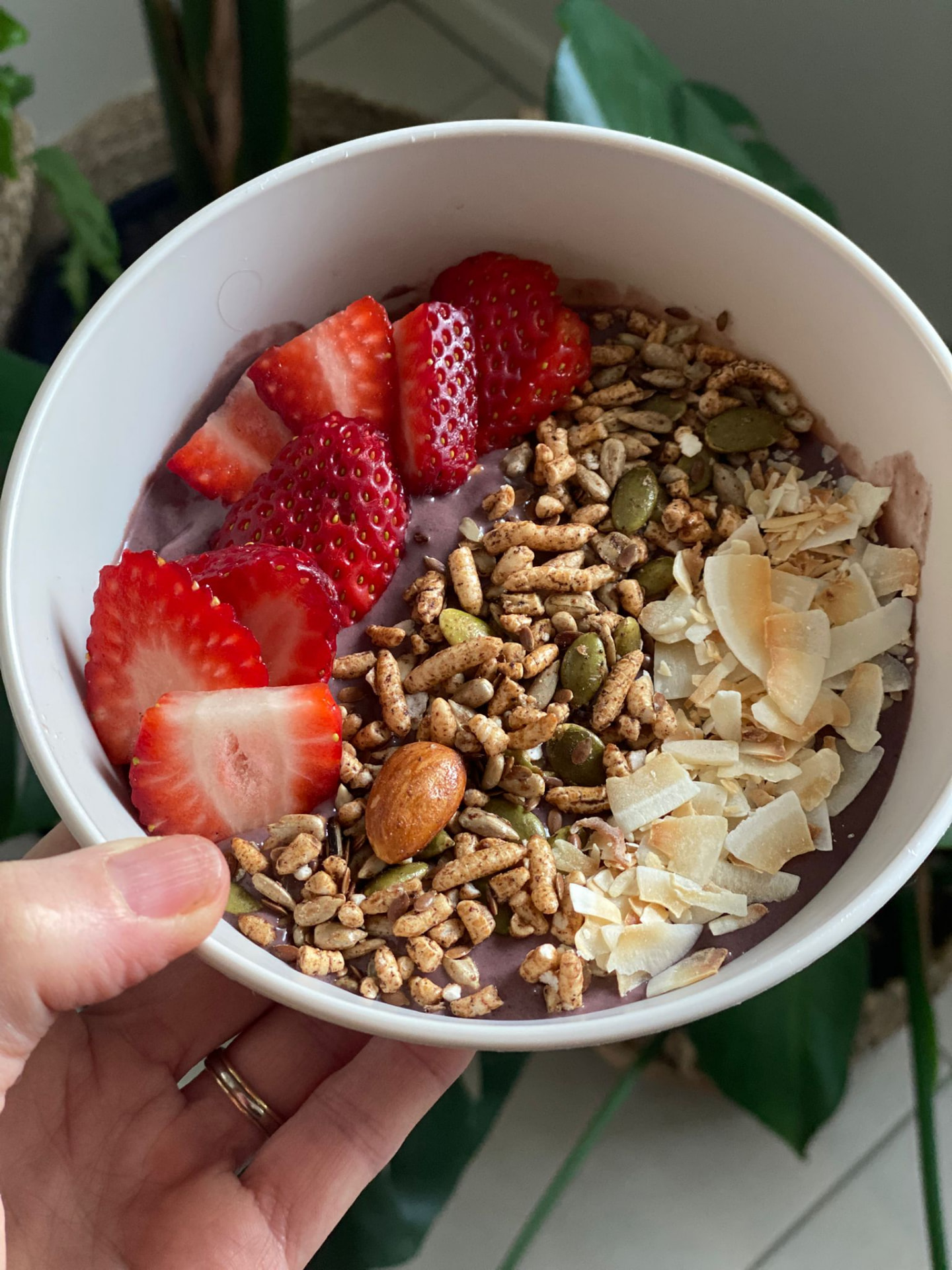 A smoothie bowl topped with strawberries, granola, seeds and coconut flakes